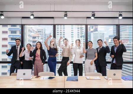 Team aziendale multietnico che festeggia il successo in un ufficio moderno nel quartiere degli affari. Uomini d'affari in piedi in fila con braccio sollevato Foto Stock