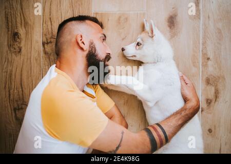Uomo sdraiato con cucciolo di Husky siberiano sul pavimento a casa Foto Stock