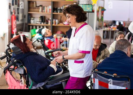 Donna caregiver che applica smalto per unghie a donna disabile in riabilitazione centro Foto Stock