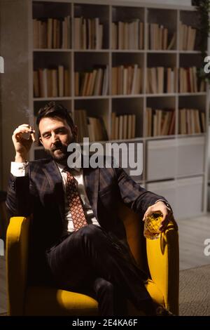 Ritratto di uomo bearded godendo di sigaro e bicchiere di whisky Foto Stock