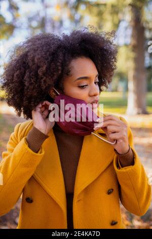 Giovane donna che rimuove la maschera protettiva mentre si sta in piedi al parcheggio Foto Stock