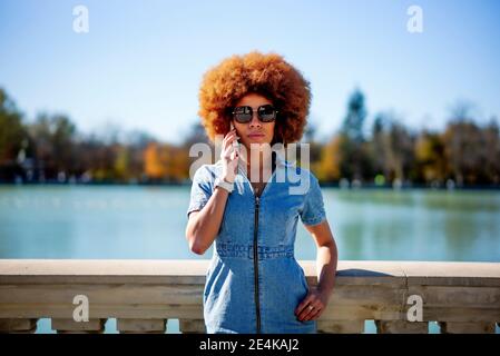 Afro capelli donna indossare occhiali da sole che parlano al telefono a Estanque Grande del Retiro stagno il giorno di sole, Spagna Foto Stock