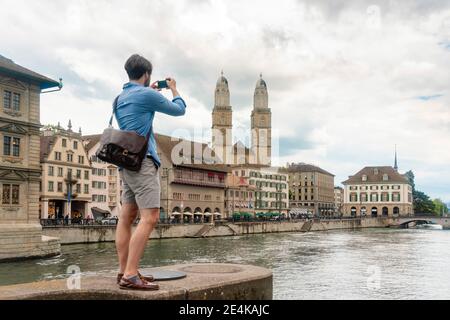 Svizzera, Zurigo, uomo che fotografa il fiume Limmat e gli edifici della città vecchia Foto Stock