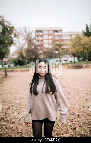 Ragazza adolescente sorridente in piedi sulla terra nel parco durante l'inverno Foto Stock