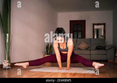 Giovane donna con gambe separate che si equilibrano sul tappetino a casa Foto Stock