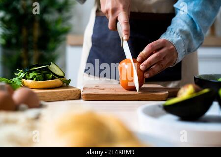 Mani di donna che affettano il pomodoro sul tagliere Foto Stock