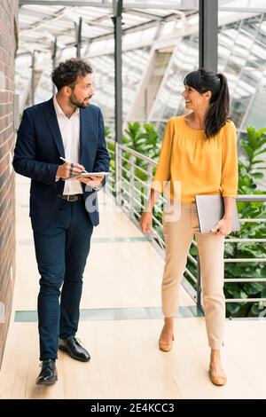 Sorridente colleghi professionisti che discutono mentre camminano in corridoio Foto Stock