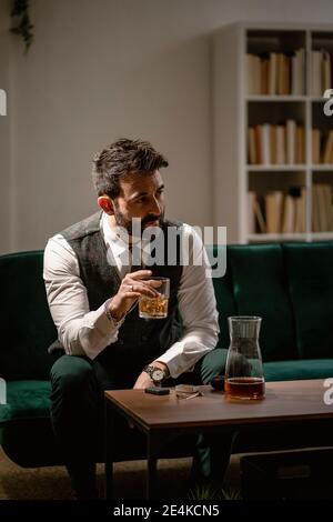 Ritratto di uomo ben vestito che beve whisky in soggiorno Foto Stock