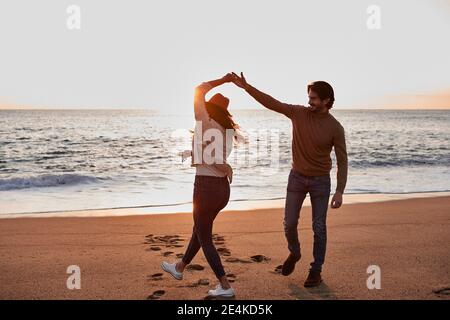 Felice giovane coppia che danzano mentre si alza in spiaggia durante l'alba Foto Stock