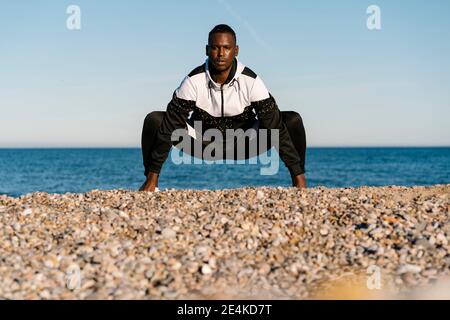 Giovane uomo che si esercita sulla spiaggia rocciosa Foto Stock