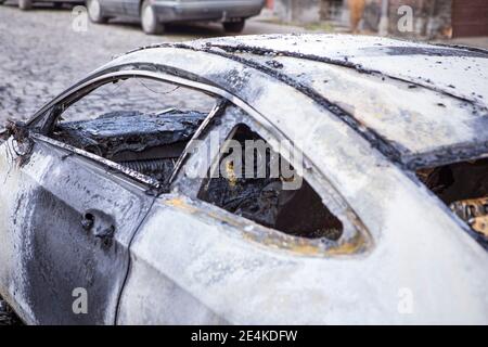Primo piano dell'auto bruciata. Auto dopo il fuoco vista laterale, crimine di vandalismo, rivolte. Auto Arson, traffico sul lato sinistro. Incidente, esplosione. Foto Stock