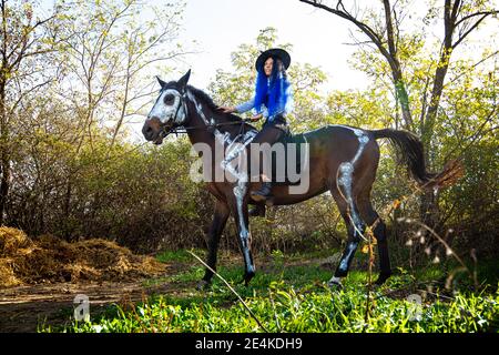 Una ragazza vestita come una strega cavalca un cavallo che uno scheletro è dipinto in vernice bianca Foto Stock