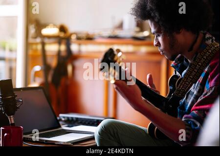 Musicista maschile sorridente che suona la chitarra in salotto Foto Stock