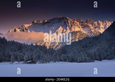 Vista panoramica della foresta innevata contro le montagne al tramonto Foto Stock