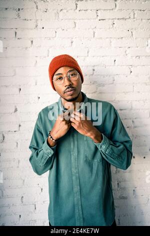 Uomo sicuro che indossa un cappello a maglia contro una parete di mattoni bianchi Foto Stock