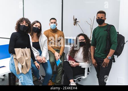 Colleghi di sesso maschile e femminile che indossano una maschera protettiva contro il bianco parete in ufficio Foto Stock