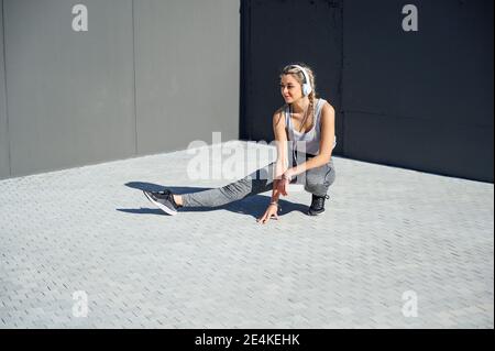 L'atleta indossa cuffie che si allungano mentre si accovacciano sul sentiero Foto Stock