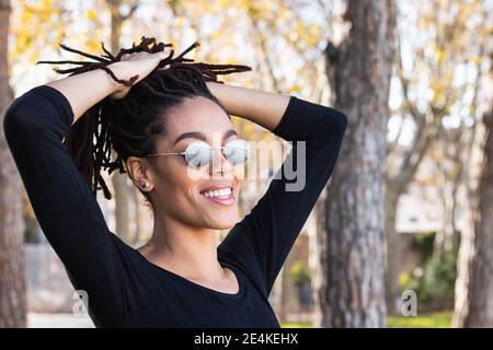 Giovane donna alla moda che indossa occhiali da sole con le mani in dreadlock a. parcheggio Foto Stock
