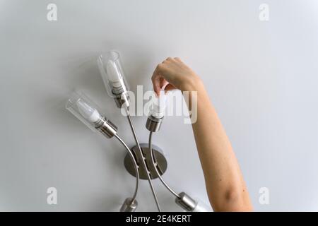 un uomo cambia una lampadina bruciata in un lampadario. mano da vicino Foto Stock