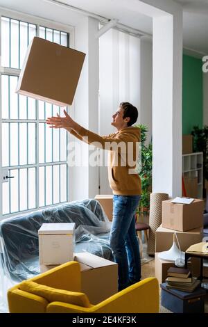 Un giovane uomo divertente che lancia una scatola di cartone mentre si passa al nuovo casa Foto Stock