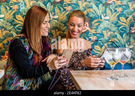 Ritratto di due donne sedute insieme al tavolo del ristorante usando smartphone Foto Stock