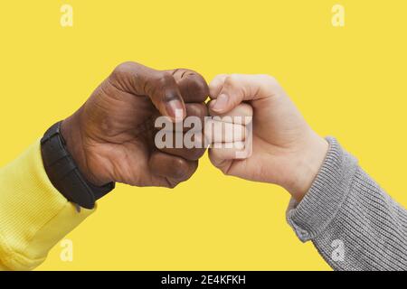 Primo piano grafico di due giovani che battono pugni contro sfondo giallo illuminante, amicizia interrazziale e concetto di unità, copia spazio Foto Stock
