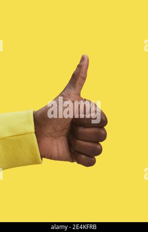 Grafico primo piano della mano maschio afroamericana che mostra i pollici verso l'alto gesto su sfondo giallo, copia spazio Foto Stock