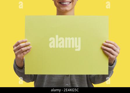 Immagine grafica di sfondo di una donna sorridente che tiene carta bianca contro sfondo pop giallo, mock up, copia spazio Foto Stock