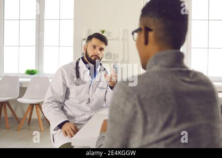 Uomo medico terapeuta seduta e parlando con paziente uomo nero in clinica Foto Stock