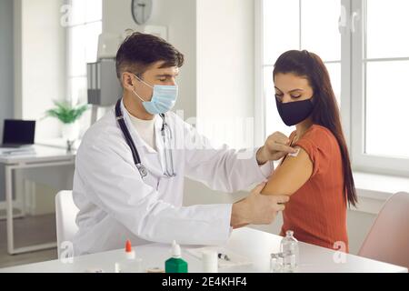 Medico in uniforme bianca e maschera medica che aderisce cerotto sterile dopo l'iniezione Foto Stock