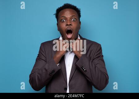 Giovane uomo africano in tuta urlando in shock, mantenendo la bocca aperta, sensazione di stress dopo aver dimenticato di pagare le bollette in tempo. Foto Stock
