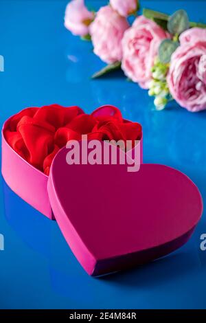 Aprire la confezione regalo a forma di cuore rosa su sfondo blu. Fiori per San Valentino, foto verticale Foto Stock