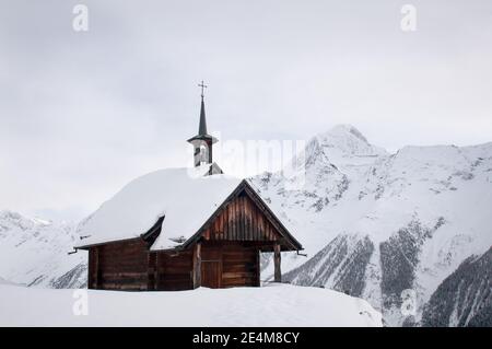 piccola cappella tradizionale coperta di neve arroccata in alto in svizzera alpi cime di montagna sullo sfondo Foto Stock