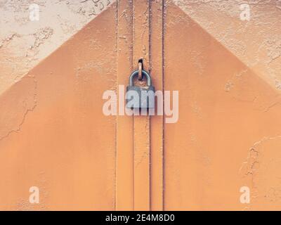 Lucchetto appeso sulle porte del garage chiuse in rosso il muro shabby della casa Foto Stock