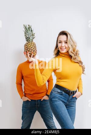 Uno scherzo. La ragazza tiene l'ananas in mano davanti alla testa del ragazzo Foto Stock