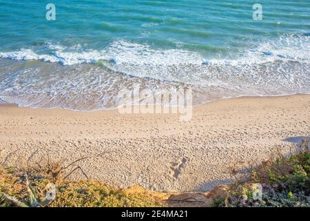 vista sopra la linea di mare, acqua di oceano e onde, con più impronte sulla sabbia della spiaggia, dalla montagna Foto Stock