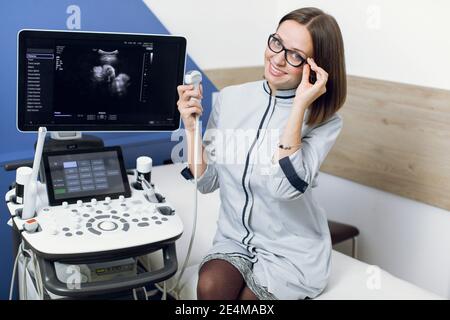 Medicina, sanità, concetto di persone. Scansione a ultrasuoni. Ritratto di giovane donna caucasica ecografa in occhiali, ecografia operatrice Foto Stock