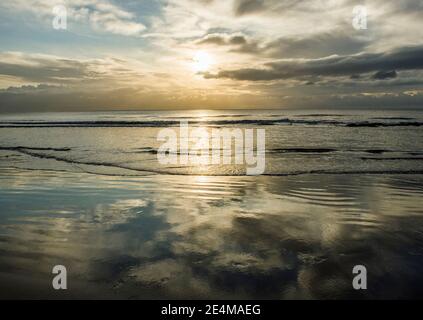 Un sole tramontante e una sabbia bagnata piena di riflessi del cielo a Dunraven Bay nel tardo pomeriggio mentre il sole comincia a tramontare. Foto Stock