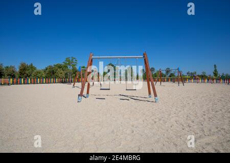 Due set di altalene sulla terra di sabbia nel parco giochi pubblico di Valdebebas nella città di Madrid, Spagna, Europa Foto Stock