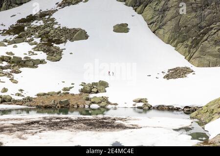 Due alpinisti lontani che camminano sulla neve sopra la Grande Laguna del Monte Penalara (Parco Naturale Guadarrama, Madrid, Spagna) Foto Stock