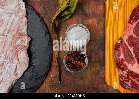 Bistecca di manzo crudo e maiale segreto su una tavola di legno da cucina e piatto rotondo ardesia su un vecchio tavolo di legno in tonalità marrone. Concetto di cibo gourmet Foto Stock