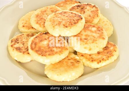 Alcune deliziose frittelle al formaggio cucinate al gusto, si trovano su un piatto leggero in ceramica. Lo sfondo è bianco. Foto Stock