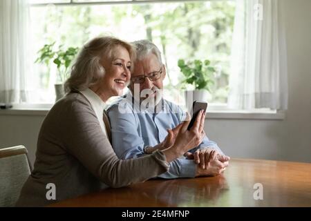 Uomo e donna felici e maturi che usano il telefono insieme, sfogliando le app Foto Stock