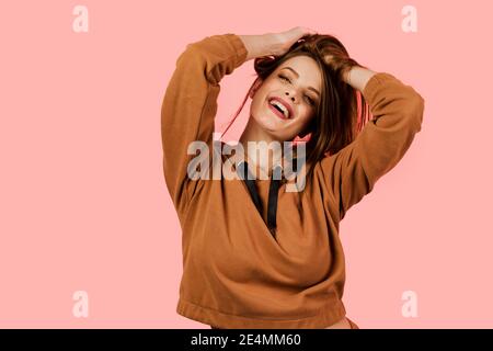 Stile di vita. Donna ispirata e felice sorride, ride e grimaces su sfondo rosa. Modello in posa in uno studio fotografico. Ragazza ha weared marrone oversize Costum Foto Stock