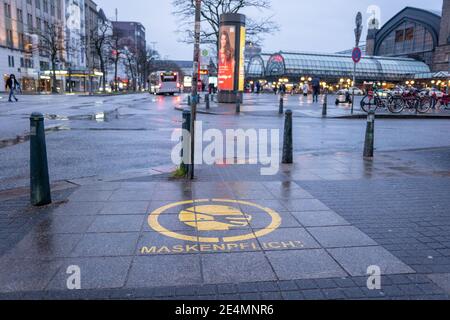 Fuoco selezionato al simbolo della maschera facciale bianca, e si prega di coprire il testo della bocca e del naso, sul segno rosso sul pavimento della stazione ferroviaria in Germania durante la socia Foto Stock
