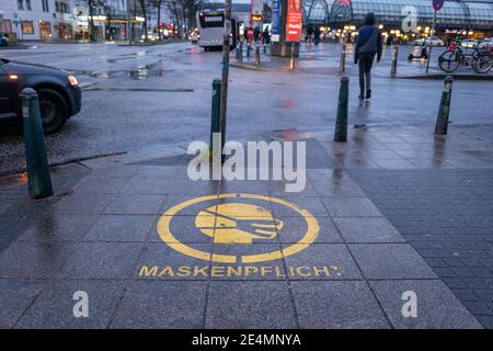 Fuoco selezionato al simbolo della maschera facciale bianca, e si prega di coprire il testo della bocca e del naso, sul segno rosso sul pavimento della stazione ferroviaria in Germania durante la socia Foto Stock