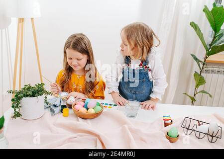 Due piccole figlie che dipingono uova di pasqua dietro un tavolo Foto Stock