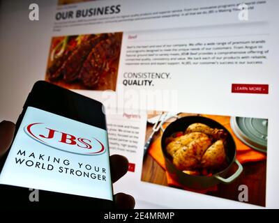 Persona titolare cellulare con logo della società brasiliana di lavorazione meet JBS S.A. in esposizione con il sito web. Concentrarsi sul centro del display del telefono cellulare. Foto Stock