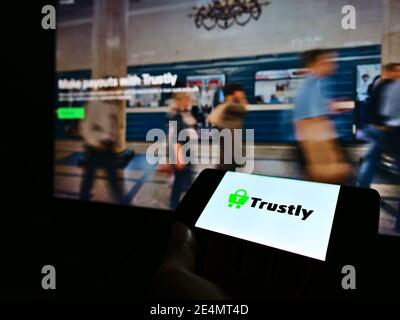 Persona che detiene smartphone con il logo della società svedese di fintech Trustly Group sullo schermo di fronte al sito web. Mettere a fuoco il centro del display del telefono. Foto Stock