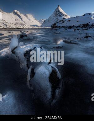 Interessanti texture ghiacciate in primo piano dell'iconica montagna Volandstind vicino a Fredvang a Lofoten, Norvegia, durante una fredda giornata di sole invernale. Foto Stock